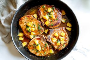 Four pineapple pork chops in a black skillet, top view.