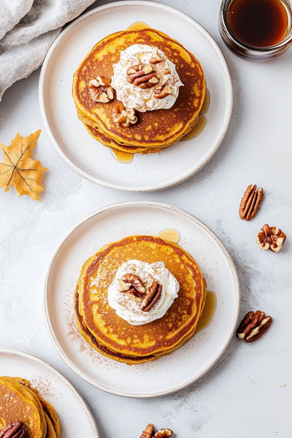 An overhead view of pumpkin spice pancakes with maple syrup on the side served on plates