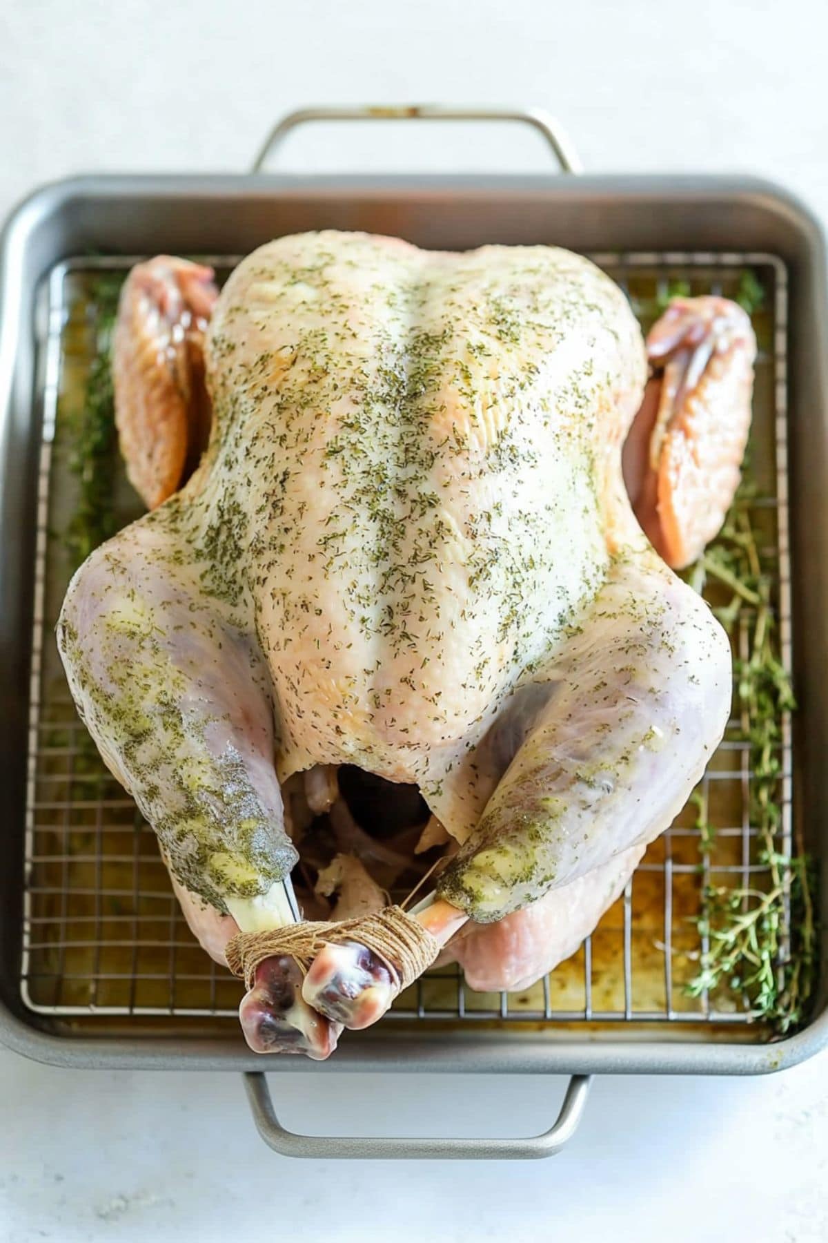 Large raw turkey rubbed with butter herbs sitting on a cooling rack.