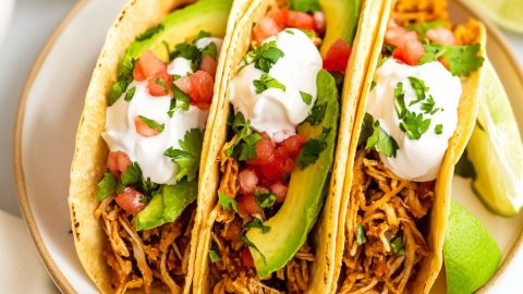 Serving of chicken tacos with sliced avocados, sour cream, chopped parsley and sour cream arranged in a plate.