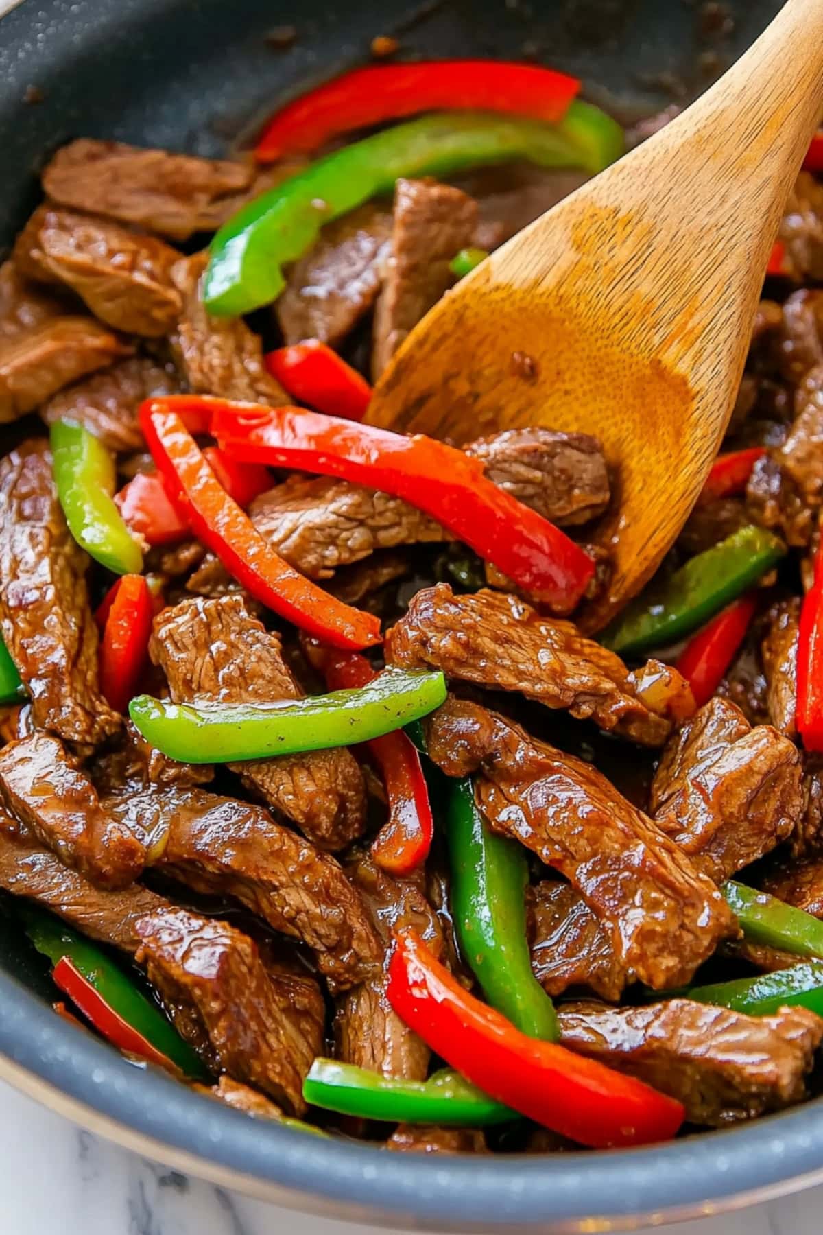 A bowl of pepper steak fry with tender beef strips, bell peppers, and onions, coated in a savory sauce.