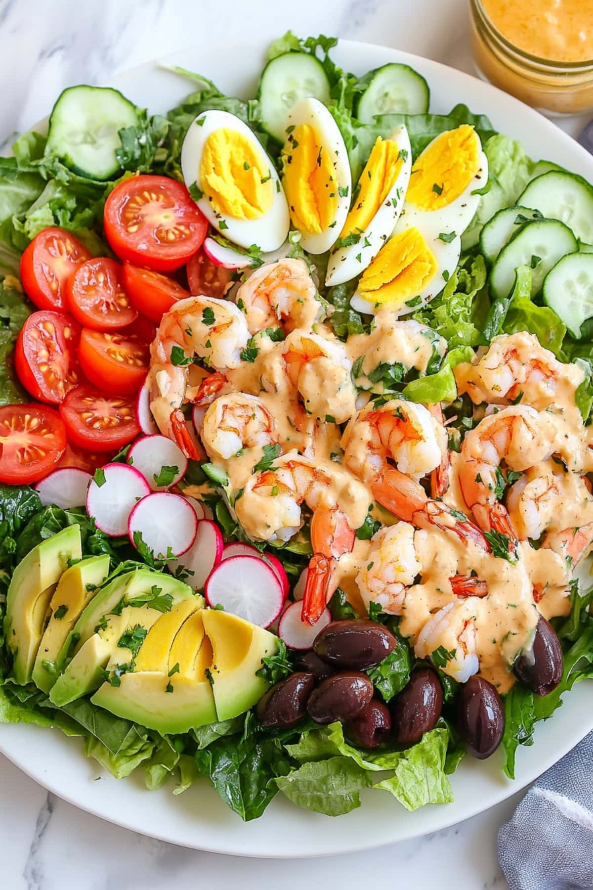 Shrimp louie salad with lettuce, tomatoes, eggs, avocados, black olives and radishes.