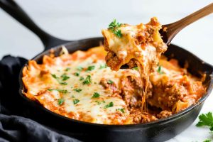 Skillet lasagna scooped with a wooden ladle.