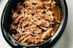 Pulled pork inside a black oval slow cooker.