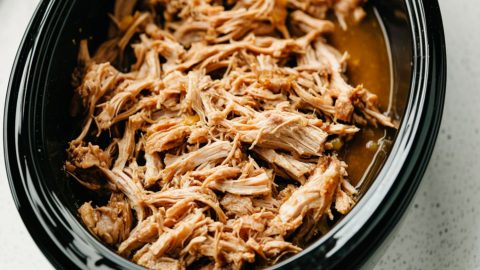 Pulled pork inside a black oval slow cooker.