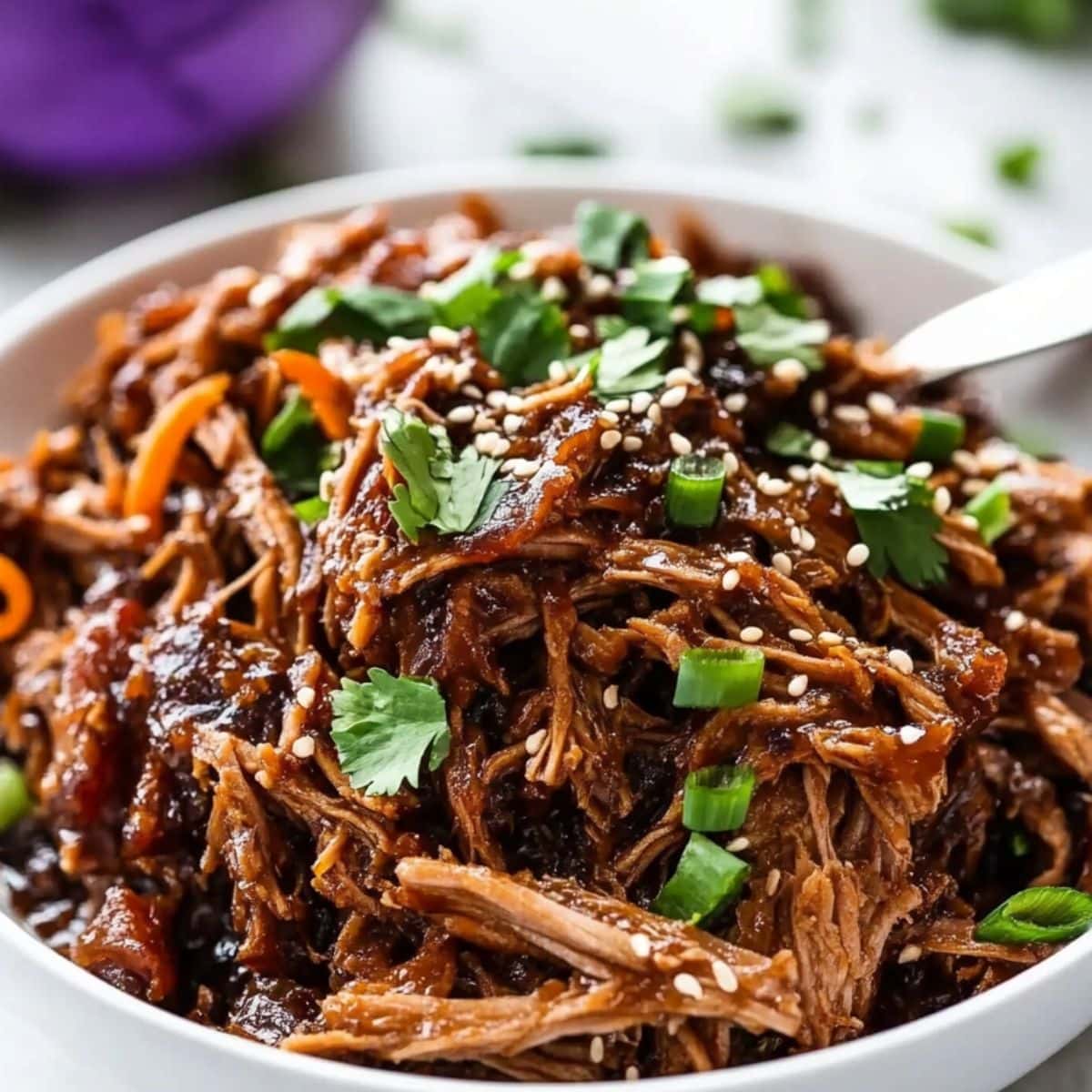 Saucy Asian pulled pork served in a white bowl, garnished with chopped scallions