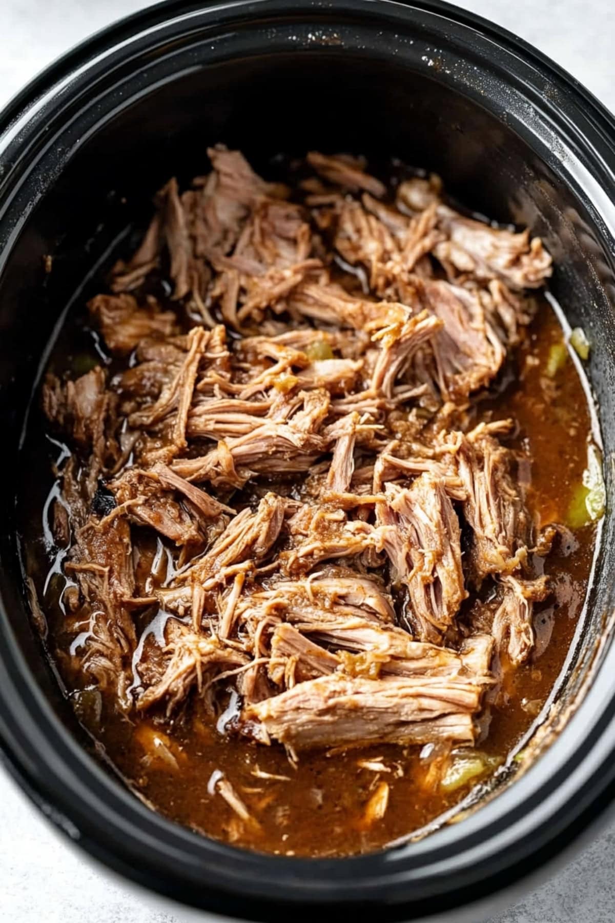 Shredded slow cooked pork in a slow cooker with juices from the spice blend.