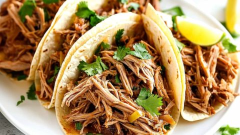 Carnitas with slow cooked shredded pork shoulder, garnished with parsley and lime slice.