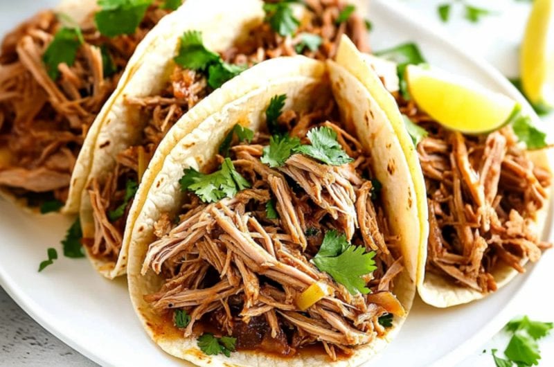 Carnitas with slow cooked shredded pork shoulder, garnished with parsley and lime slice.