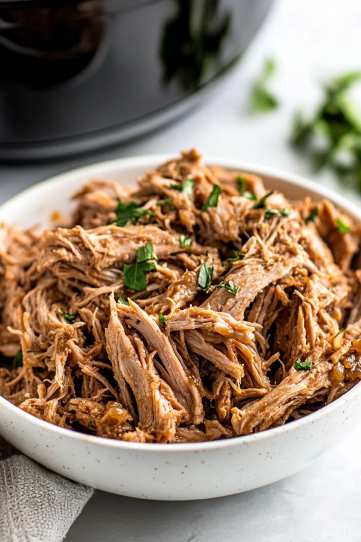 Shredded pork butt roast in a bowl with fresh cilantro.