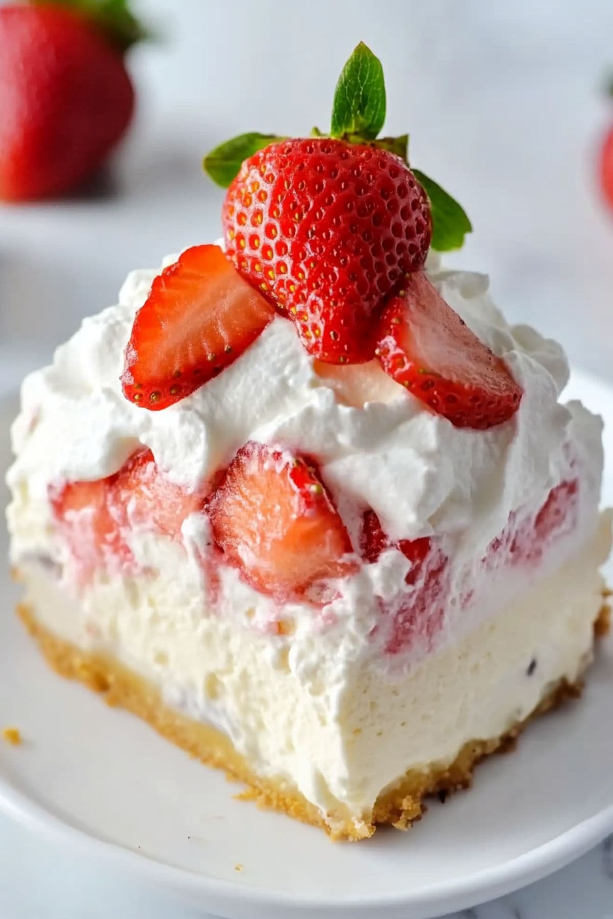 A slice of strawberry cheesecake with whipped cream and pudding garnished with fresh strawberries served on a white plate.