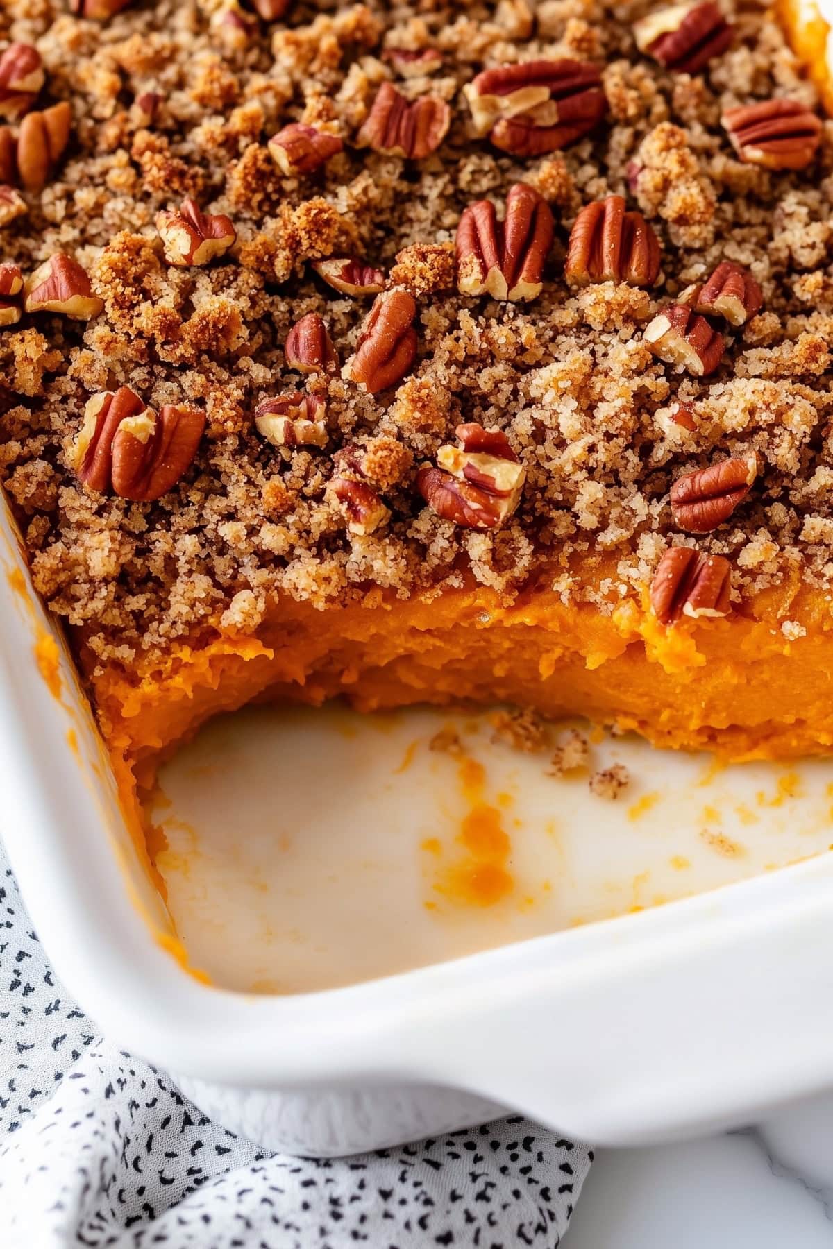 A baking dish of sweet potato souffle with streusel toppings and nuts.