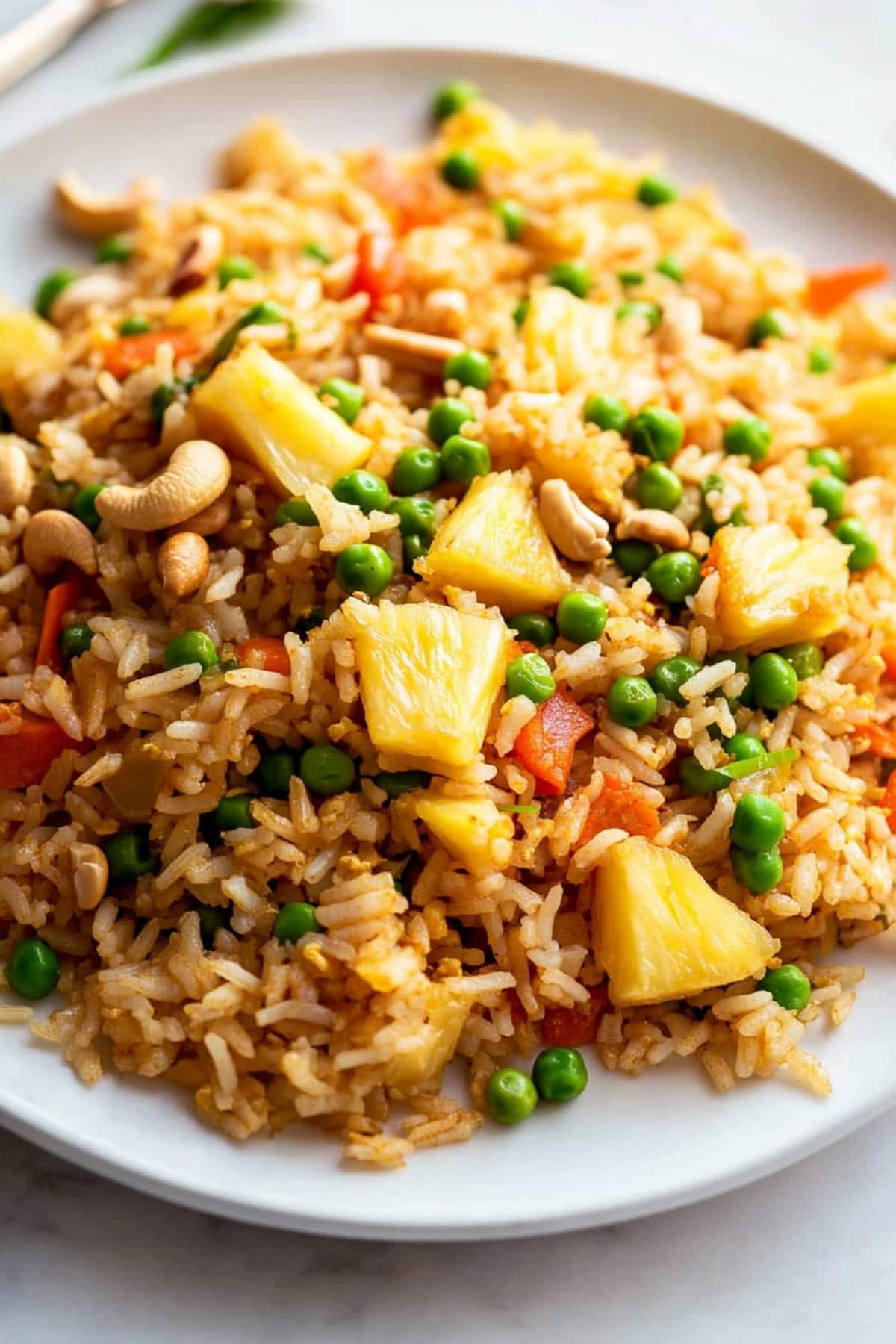 Fried rice with pineapple, carrots and green peas served in a white plate.