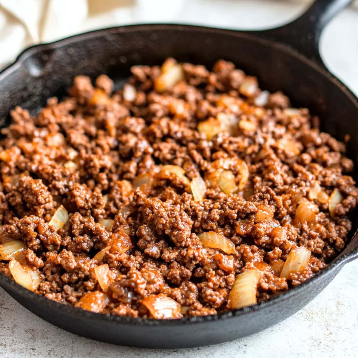 Sauteed ground beef in a cast iron skillet sitting on a white concrete table