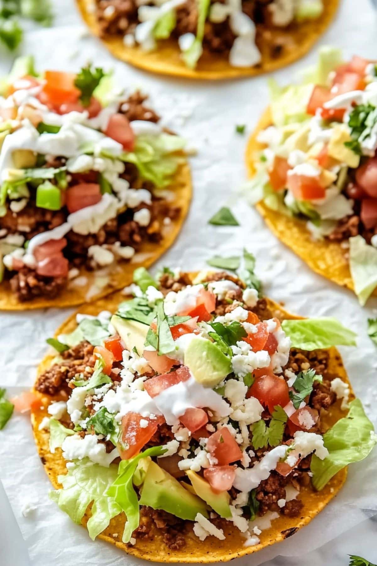 Servings of tostadas with ground beef, tomatoes, avocados, cheese and sour cream toppings.