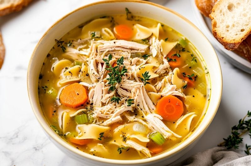 Overhead shot of a bowl of homemade turkey noodle soup, with fresh herbs and black pepper sprinkled on top.