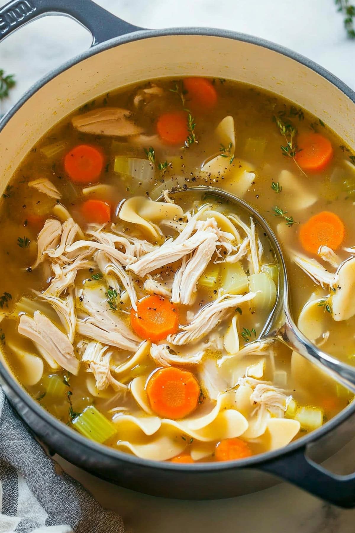 A ladle dipping into turkey noodle soup, capturing a mix of meat pieces, noodles, and vegetables in a savory broth.