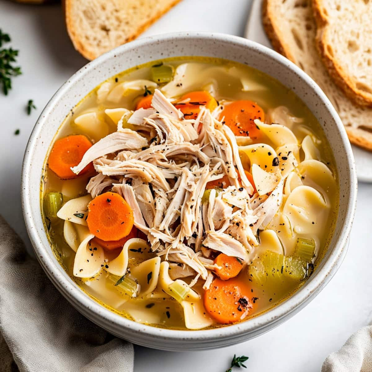 A hearty turkey noodle soup with vegetables, served with bread.