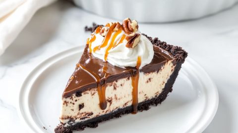 A slice serving of turtle pie with whipped cream, chopped pecans drizzled with caramel; syrup in a white plate.