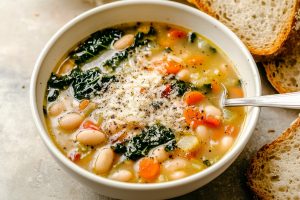 Savory homemade Tuscan white bean soup with veggies and parmesan cheese, served with bread.