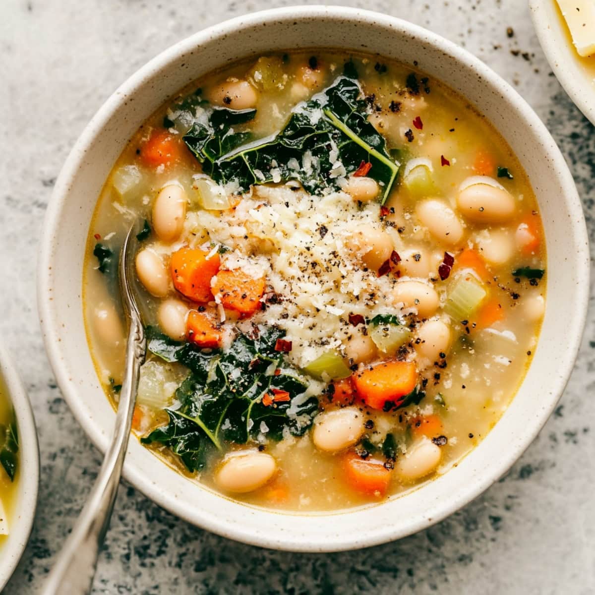 An overhead view of tuscan white bean soup with vegetables, red pepper flakes and grated parmesan.