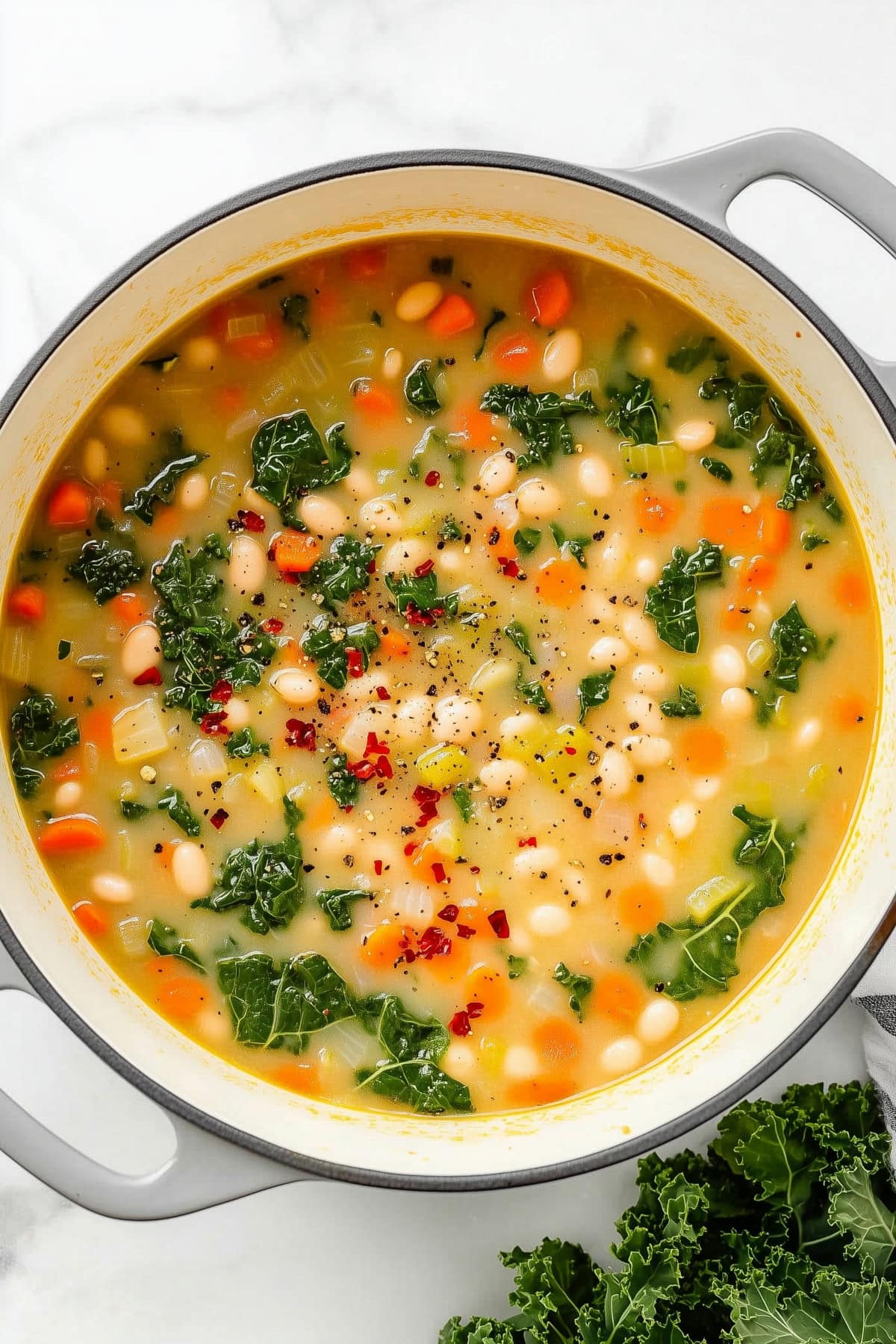 A large pot filled with Tuscan white bean soup, kale and red eppper flakes.