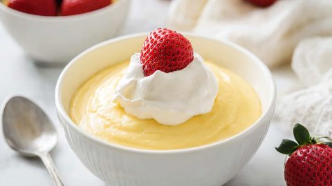 Vanilla pudding in a bowl with a dollop of whipped cream and strawberry.