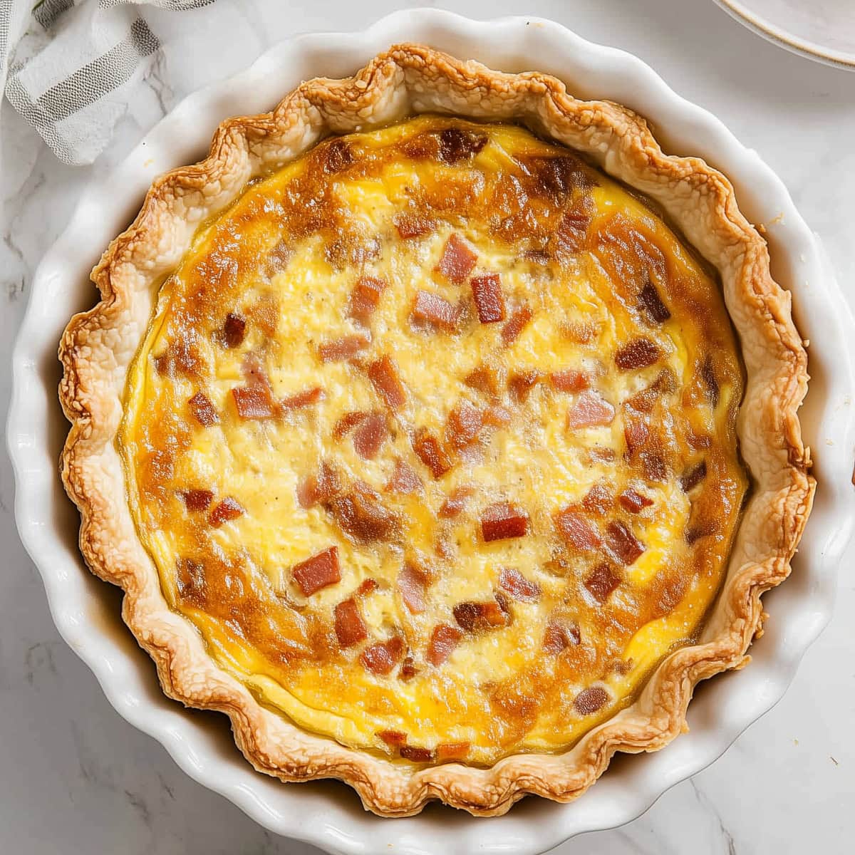 A whole bacon and cheese quiche in a pie dish.