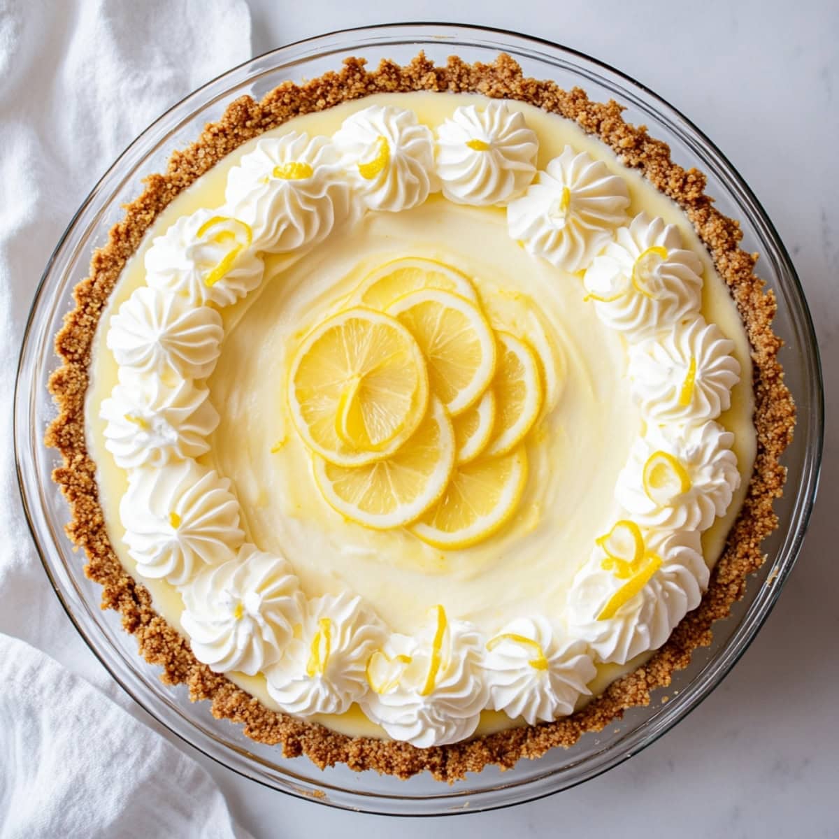 A whole lemon chiffon pie in a large pie dish on white marble table, top view