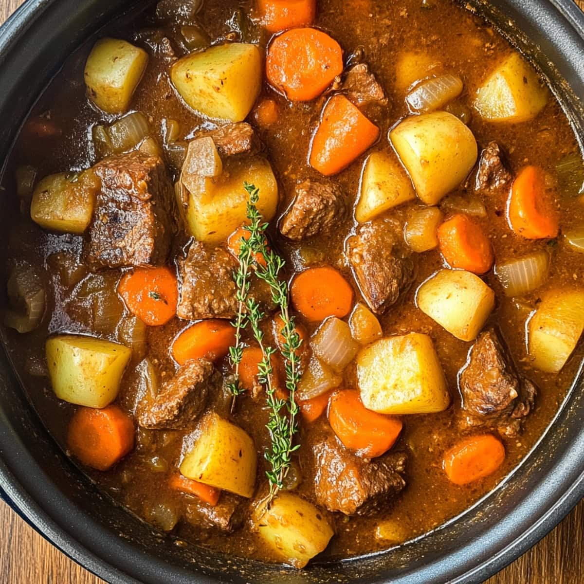 A hearty apple cider beef stew featuring slow-cooked beef, carrots and potatoes, garnished with thyme.