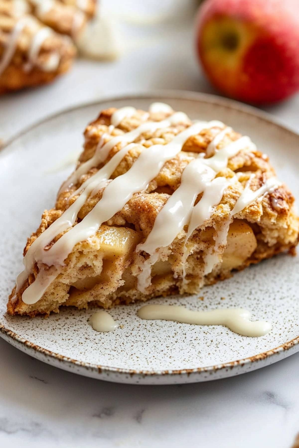 An apple cinnamon scone drizzled with vanilla glaze on a plate, side view