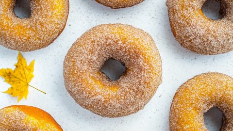 Sugar cinnamon coated pumpkin donuts flat lay on a white surface.