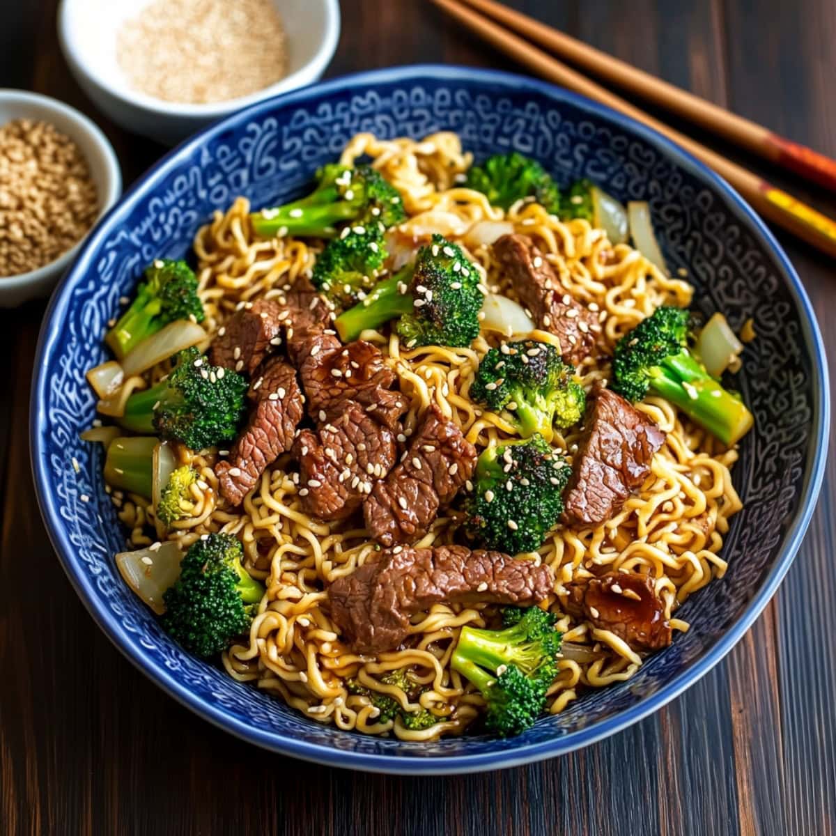 Blue bowl with serving of stir fried beef and broccoli ramen sitting on a dark wooden table.