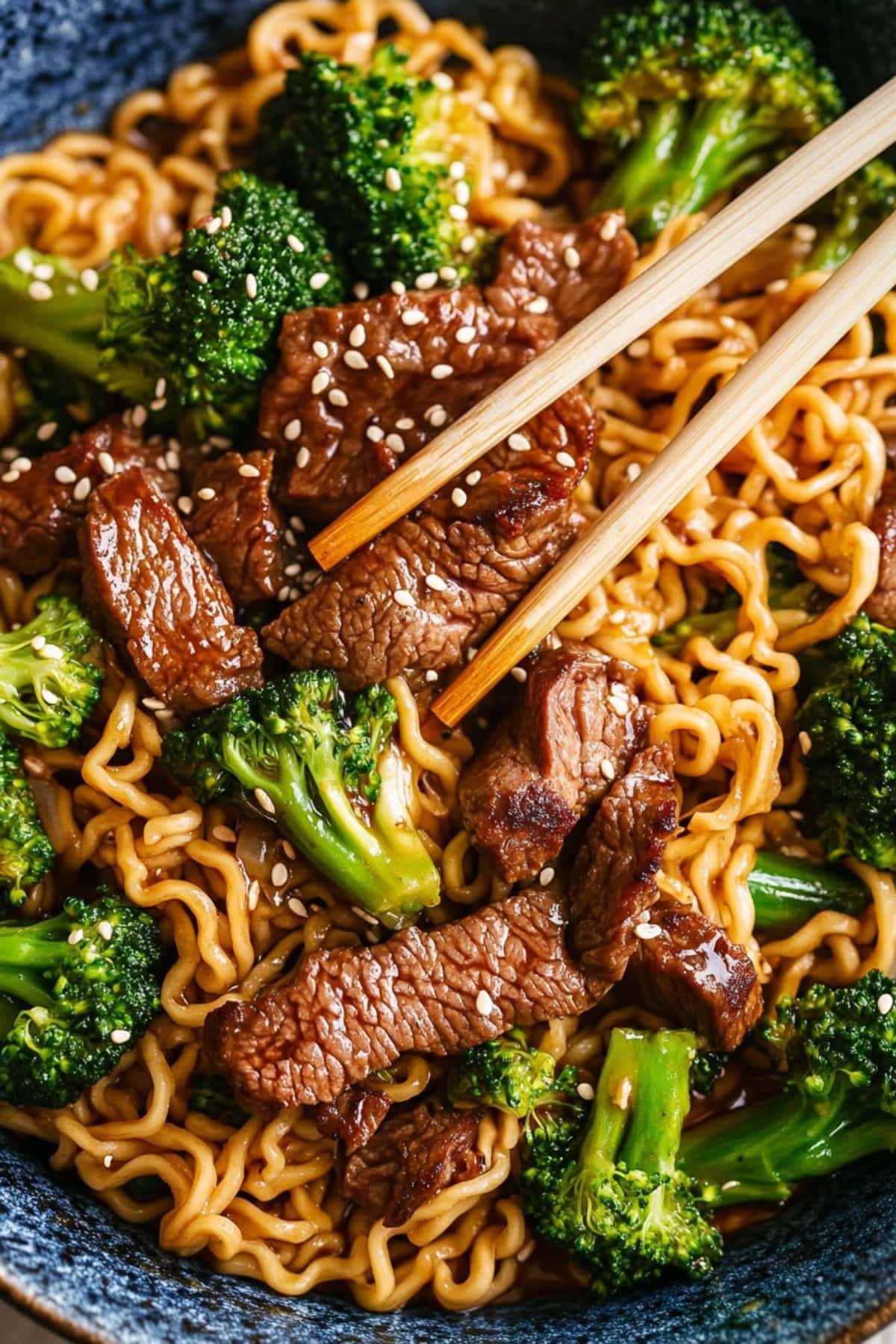 Chopsticks picking a piece of beef from serving of beef and broccoli stir fry from the bowl.