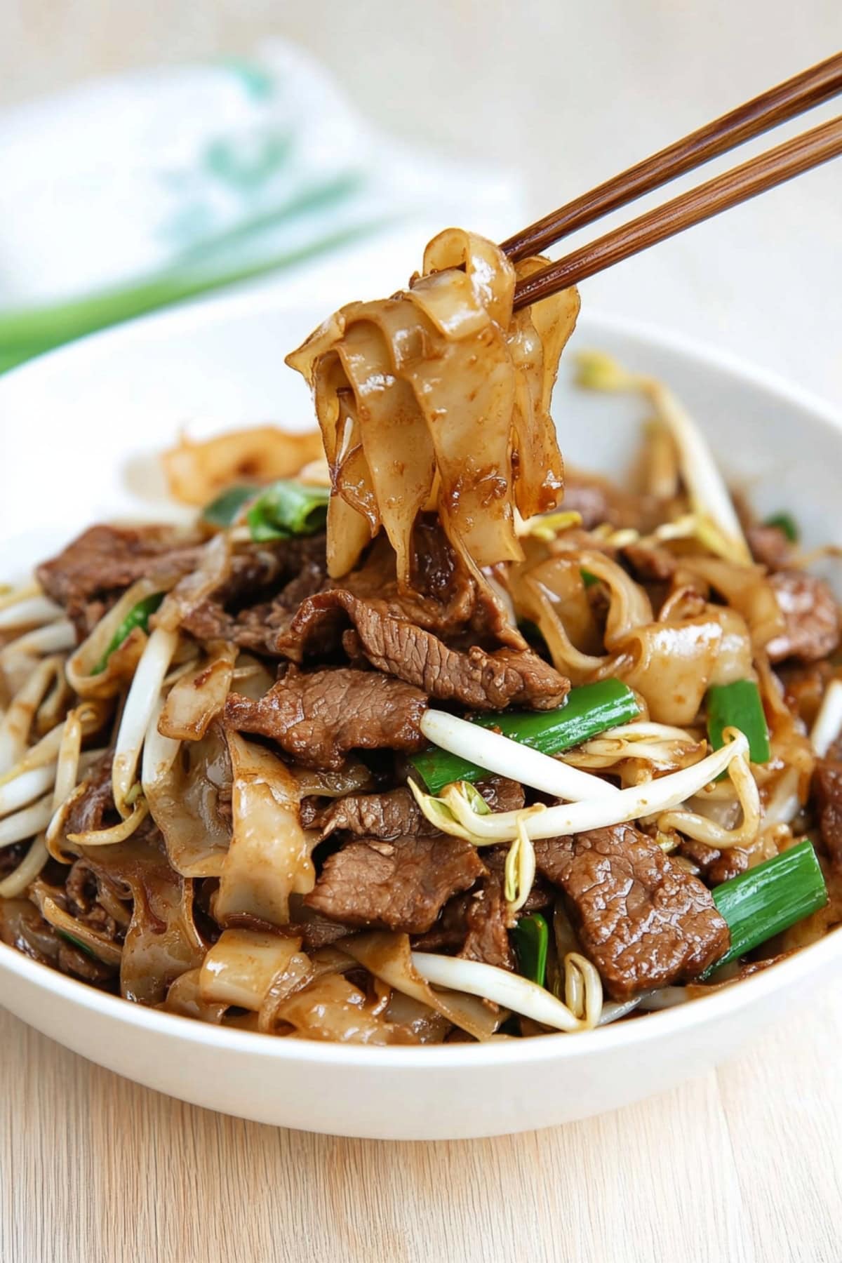 Chopsticks lifting noodles from a bowl of beef chow fun.