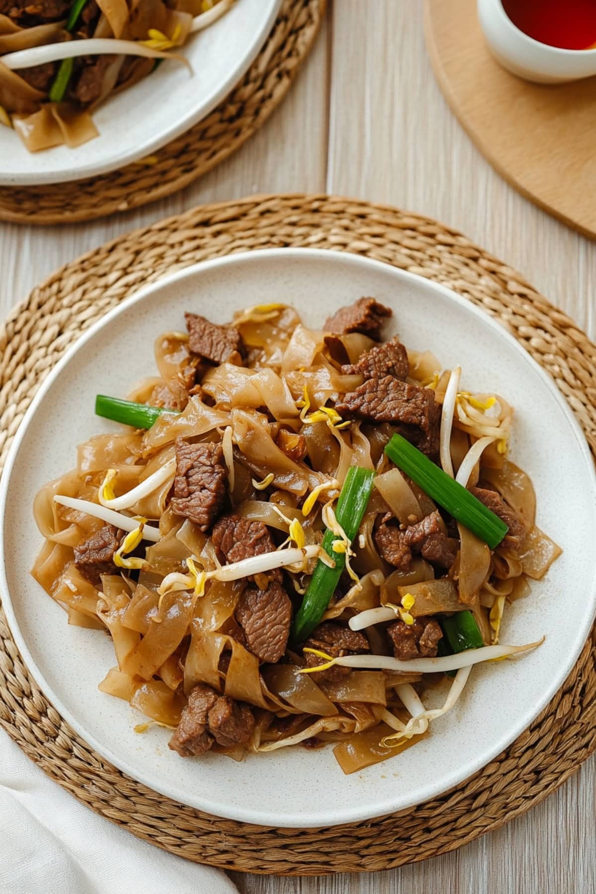 Serving of beef chow fun in a white plate made with glass noodles, beef strips and vegetables.