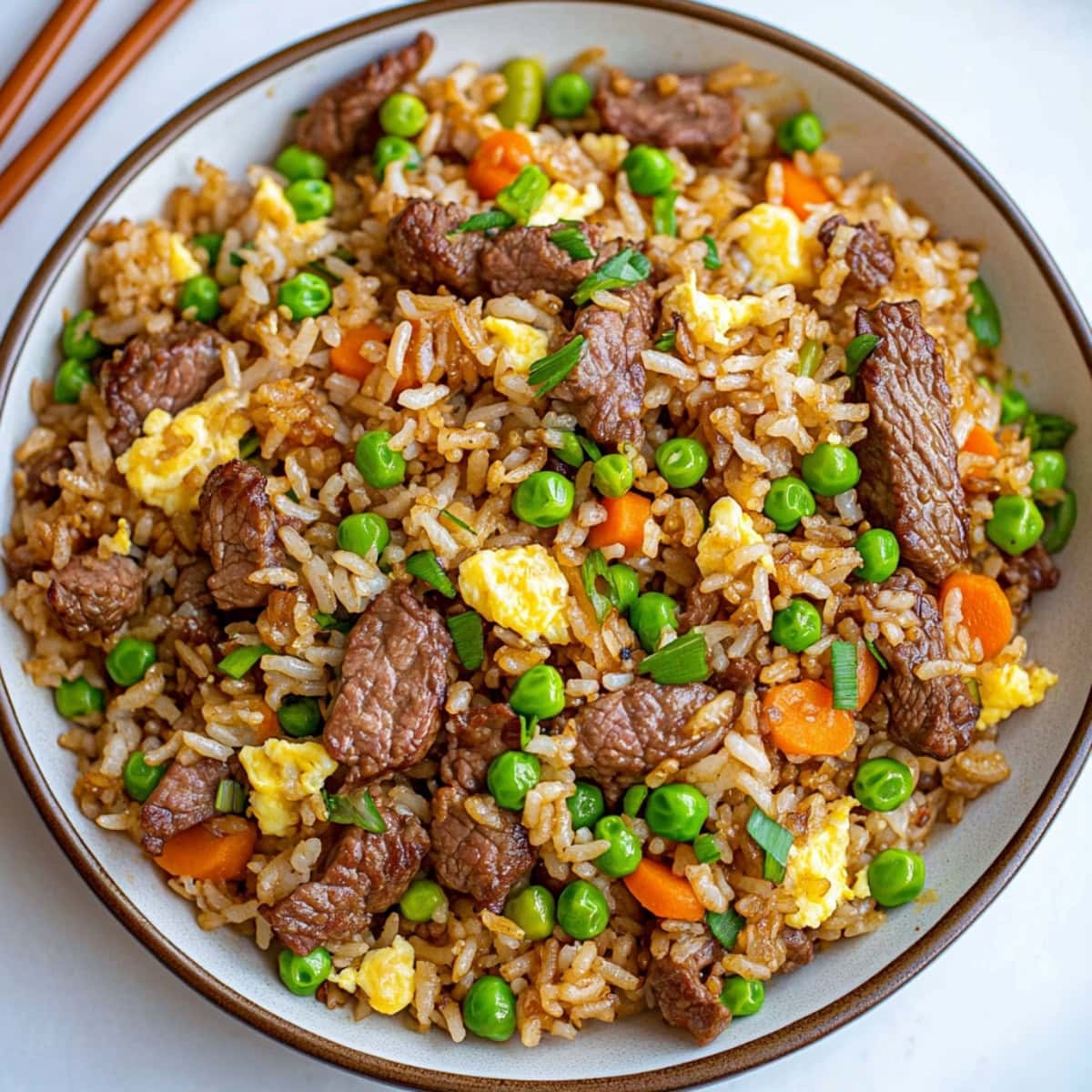 Fried rice mixed with green peas, carrots, scrambled eggs and beef strips served in a white plate.