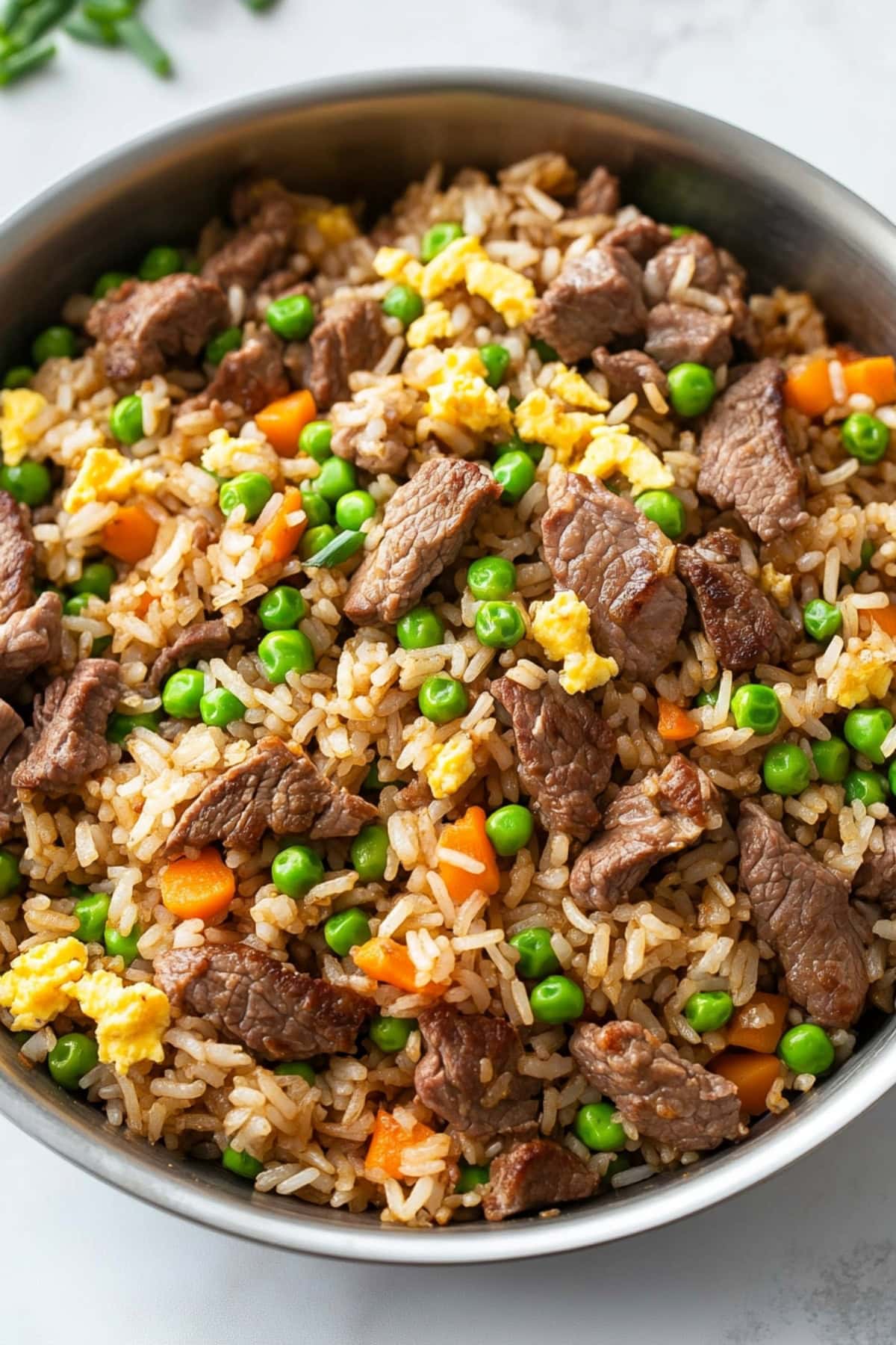 Beef fried rice in a skillet pan with beef strips, scrambled egg, carrots and green peas.