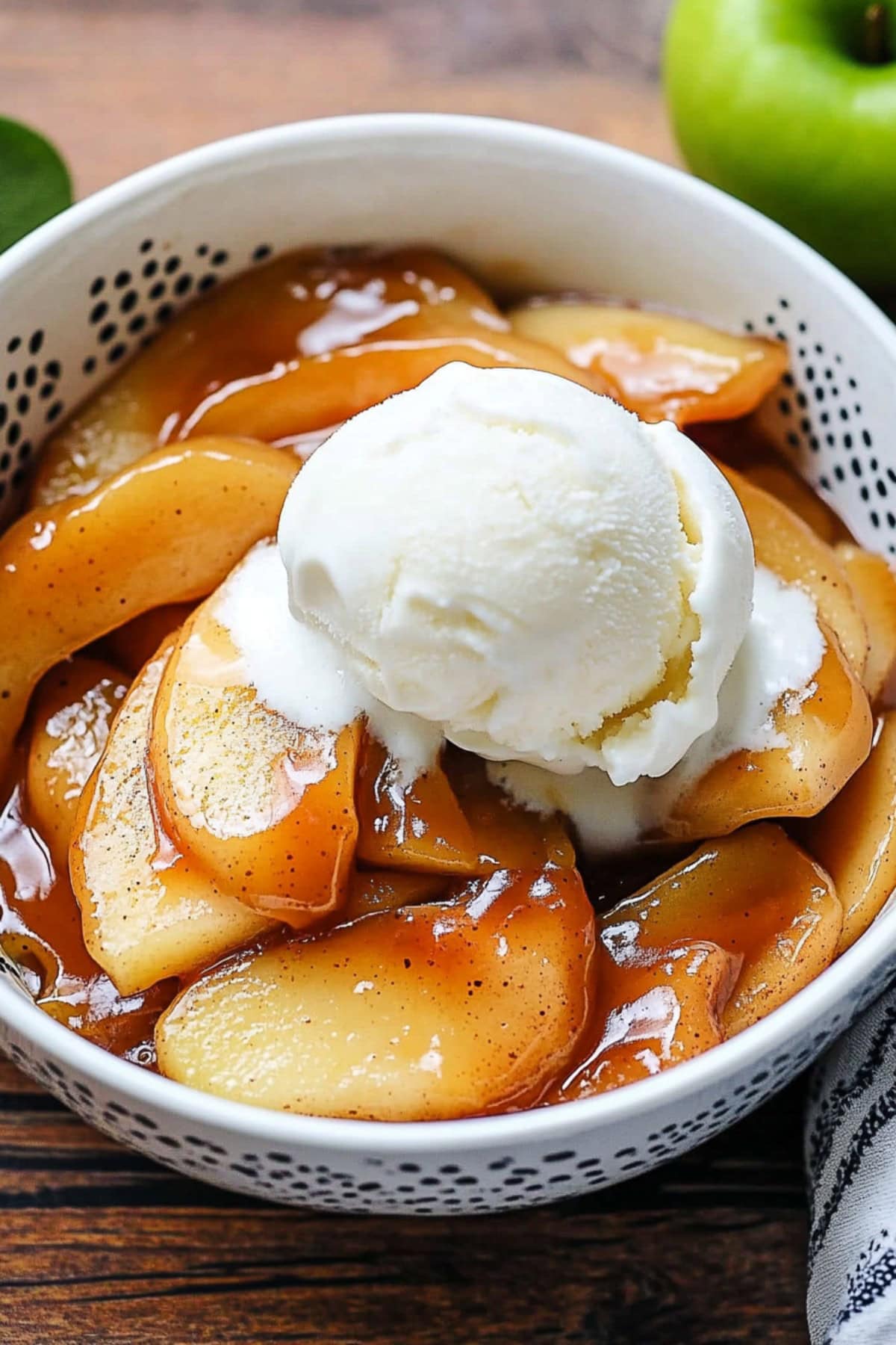 Sliced apples with caramel sauce served in a white bowl garnished with a scoop of vanilla ice cream.