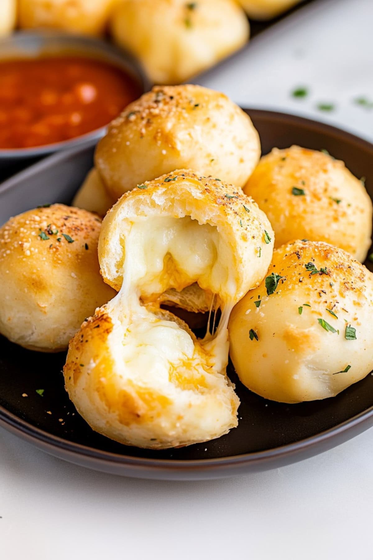 Cheese bombs sprinkled with herbs, served with a bowl of marinara sauce on the side