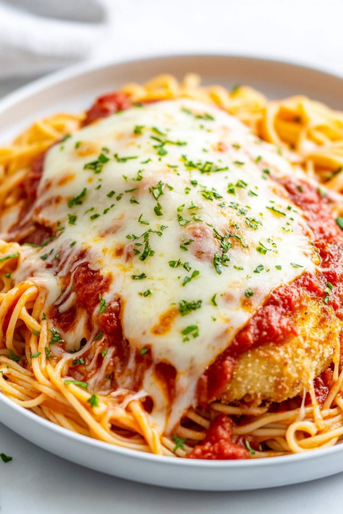 Juicy chicken cutlet breaded and fried, topped with marinara and cheese, with a garnish of parsley and served with pasta, close up