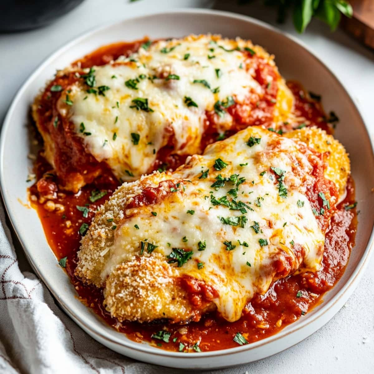 Baked chicken parmesan with melted cheese, marinara sauce and herbs on a plate