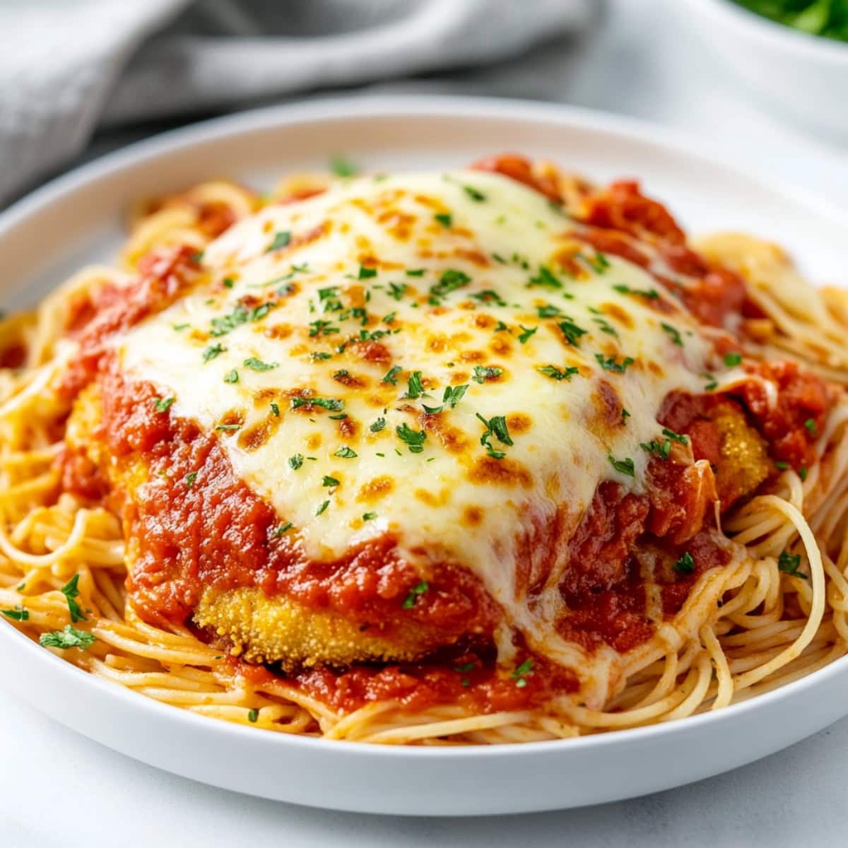 Homemade chicken parmesan on a bed of spaghetti on a white plate.