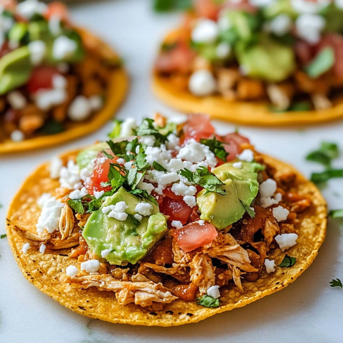 Servings of chicken tostados with crispy corn tortilla topped with refried beans, mashed avocado, shredded chicken, lettuce, tomato, red onion, cotija cheese and cilantro.
