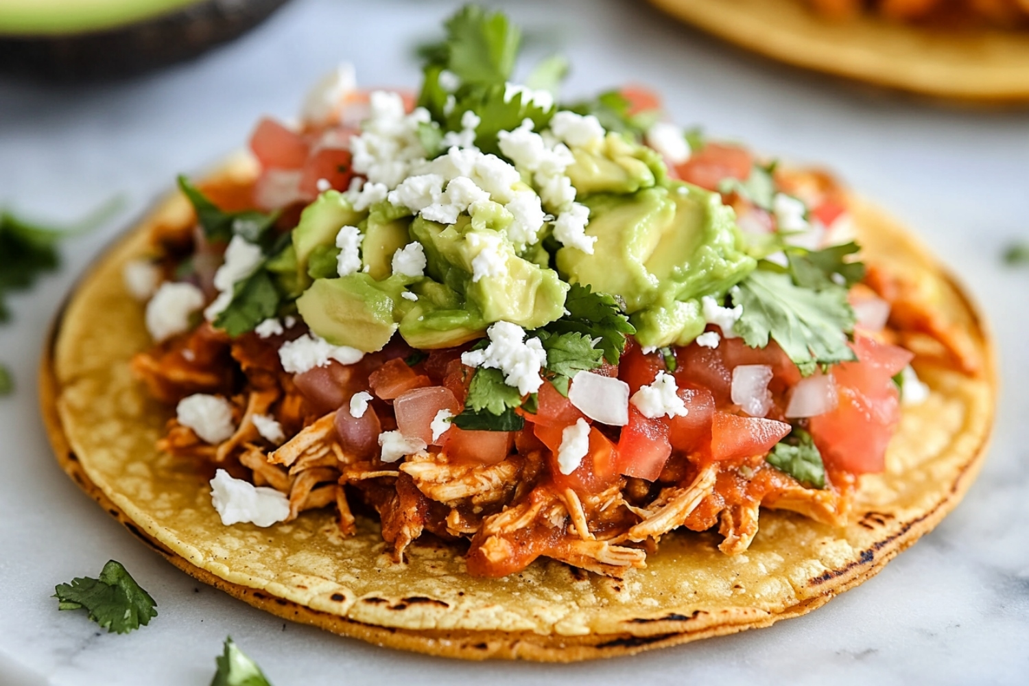 Corn tortillas topped with refried beans, mashed avocado, shredded chicken, lettuce, tomato, red onion, cotija cheese and cilantro flat lay on a marble table.