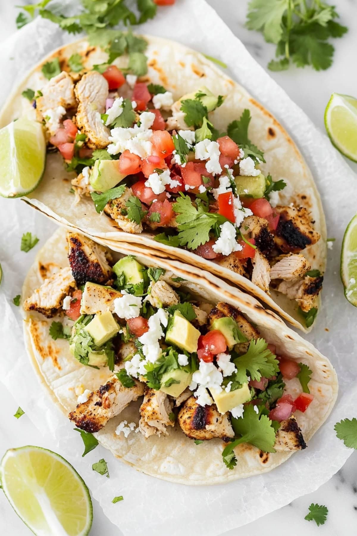 Two cilantro lime chicken tacos garnished with fresh cilantro and lime wedges on a parchment paper.