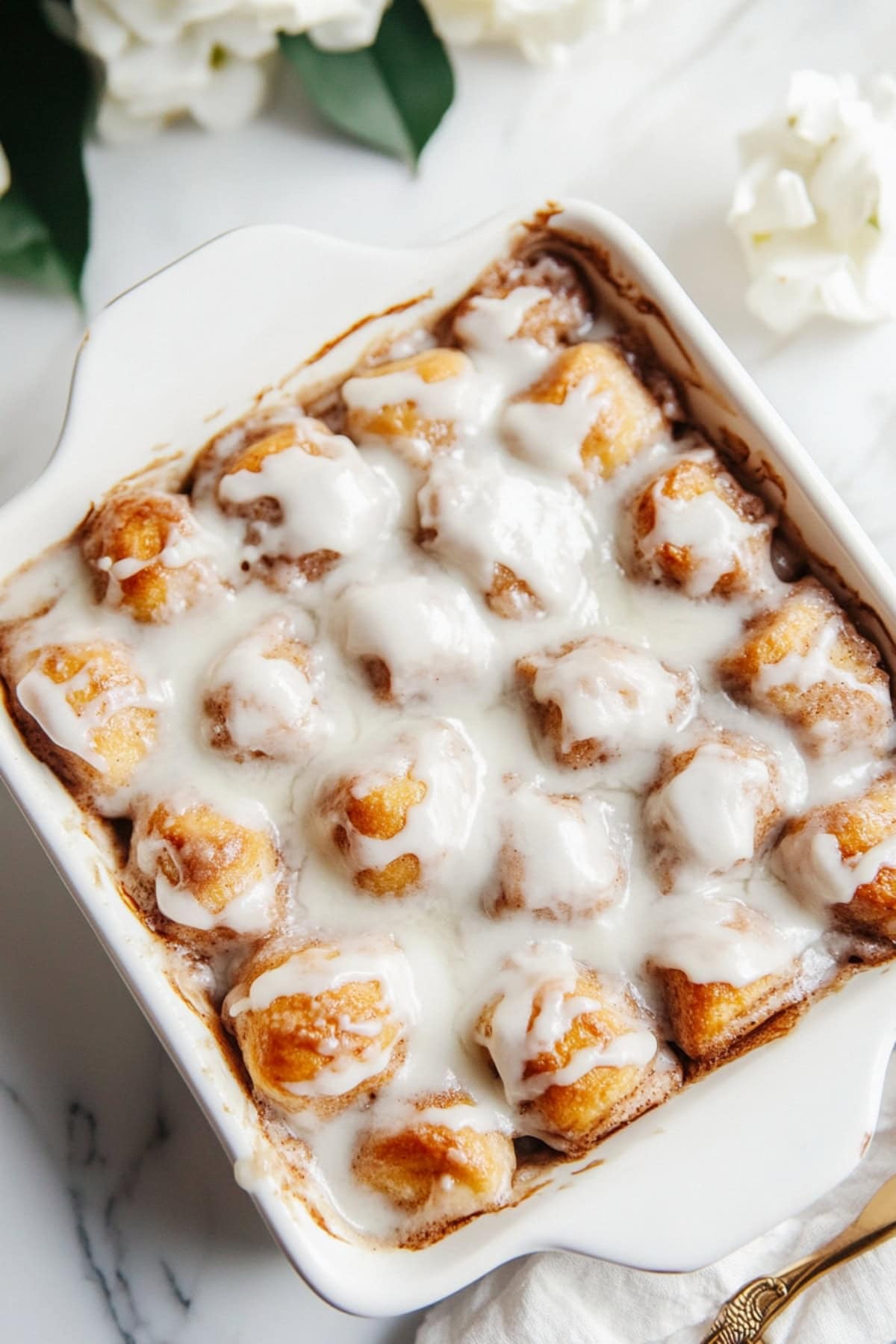 Fluffy biscuit chunks coated in cinnamon-sugar and sweet glaze in. ceramic baking dish, top view .