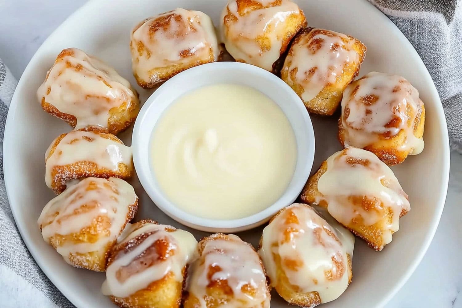 Cinnamon roll bites in a plate with vanilla glaze in the middle.