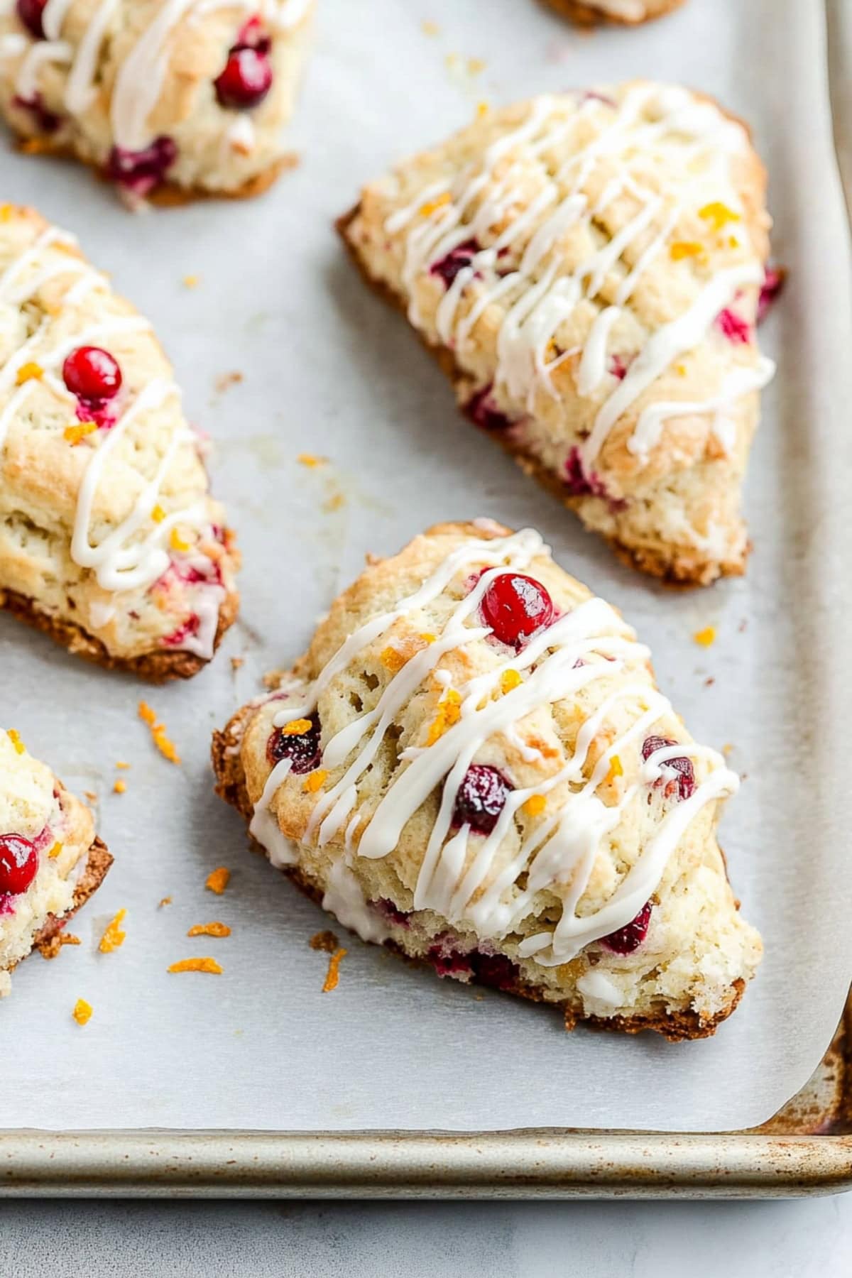 Flaky and buttery homemade cranberry orange scones on a baking tray with orange glaze drizzled over the top.