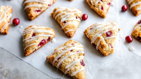 Delicious homemade cranberry scones drizzled with glaze on a parchment paper.